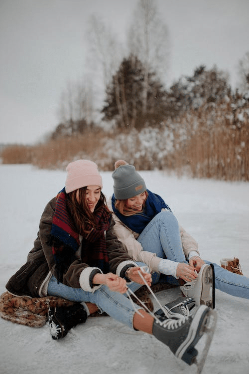 two students tightening their laces in the middle of ice skating