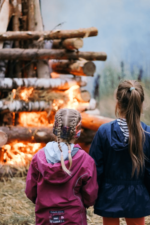 two young girls standing in front of a bonfire