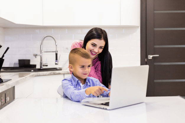 a boy smiling as he interacts with his teacher and peers during online school