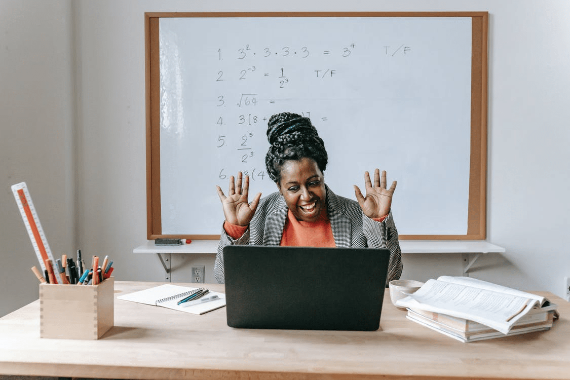 a teacher animatedly waving to her students during an online class