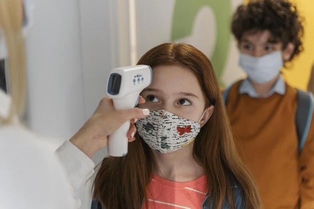 a teacher taking a young girl’s temperature before she enters class