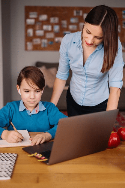 a young boy attending online school as his mother watches on