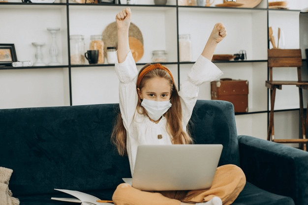 a young girl raising her arms in excitement before her online class